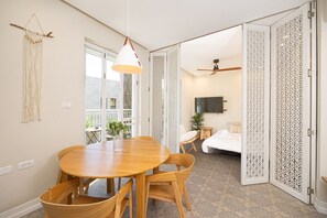 Una habitación con una mesa de comedor de madera, sillas, una lámpara colgante, una cama, un ventilador de techo y paneles decorativos.