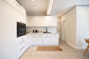 A modern kitchen with white cabinetry, a black stove, and a wooden chair.