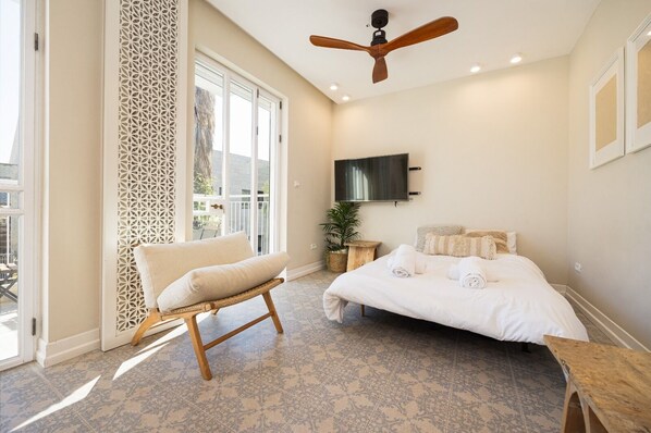 A bedroom with a bed, a chair, a TV, and a balcony.