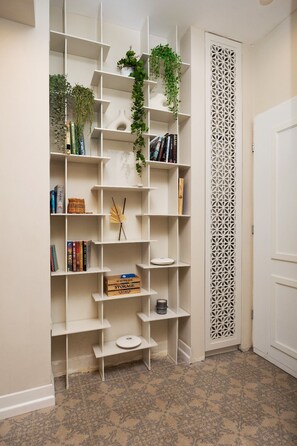 A white bookshelf with plants and books, a patterned floor, and a decorative door.
