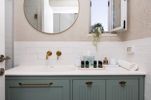 A bathroom with a white sink, gold faucets, a round mirror, a window with a plant, and a towel on the counter. - Exclusive&Lovely Apartment in Prestigious Talbiya (Jerusalem)