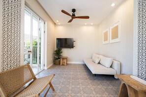 Una sala de estar moderna con ventilador de techo, un sofá, una silla de mimbre, una mesita de madera y una planta en maceta.