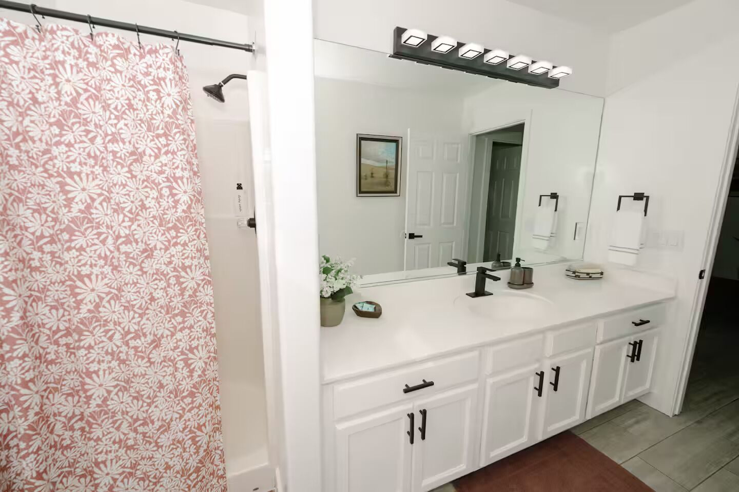 A bathroom with a shower curtain, a large mirror, a sink, and cabinets.