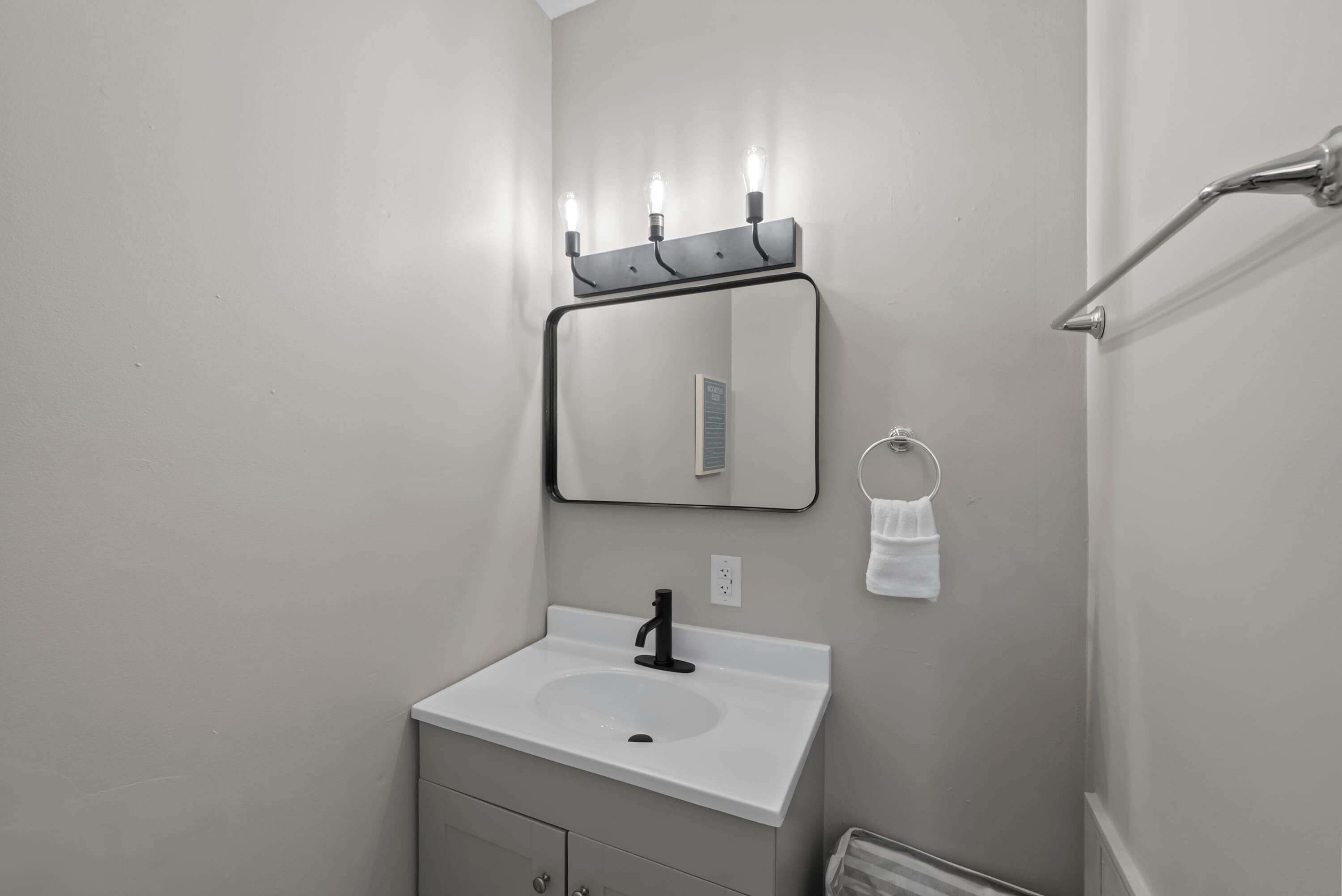 Un baño con un lavamanos blanco, un espejo con iluminación y un perchero para toallas.