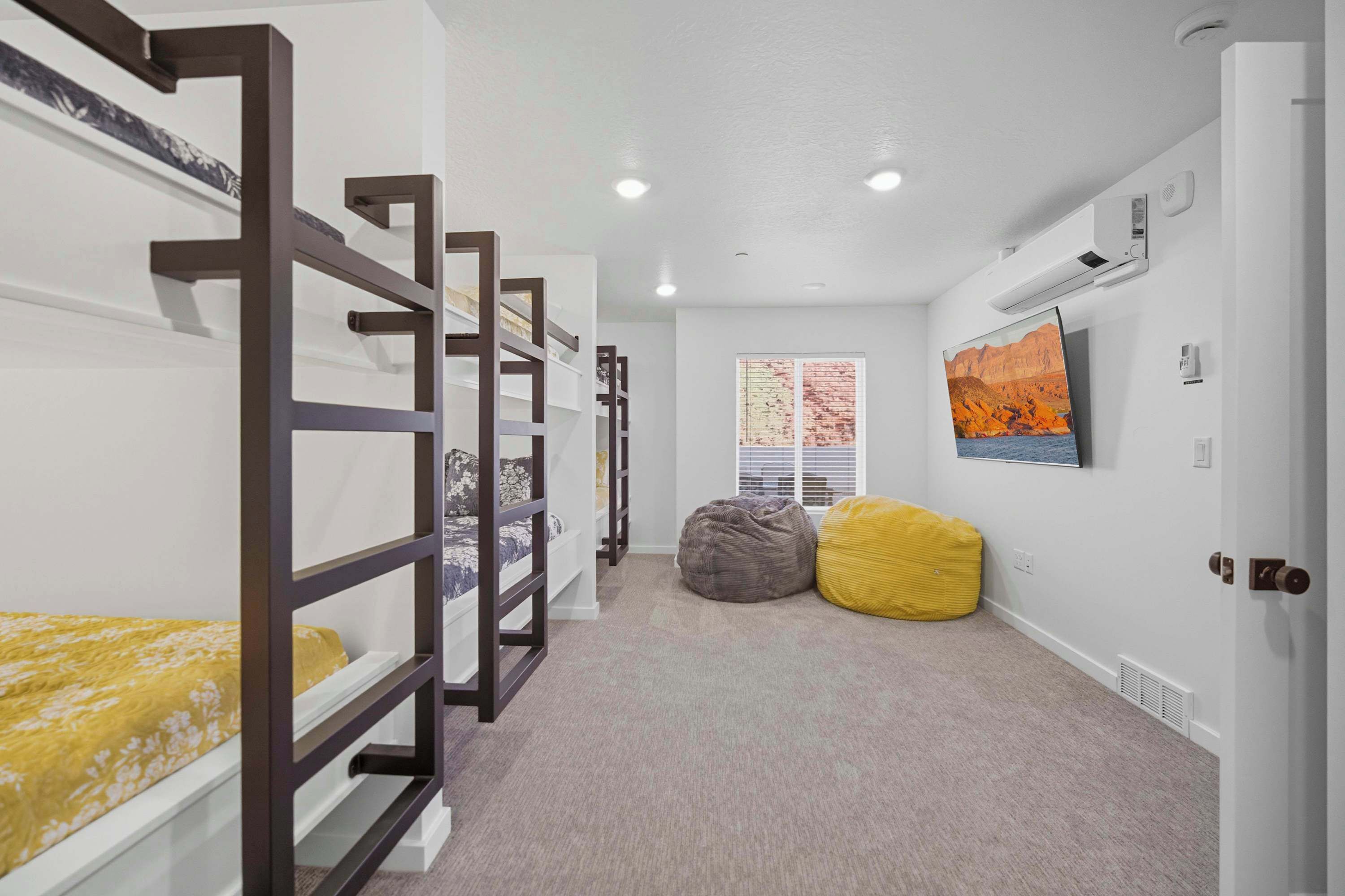A room with bunk beds, a window with blinds, a painting, and a door.