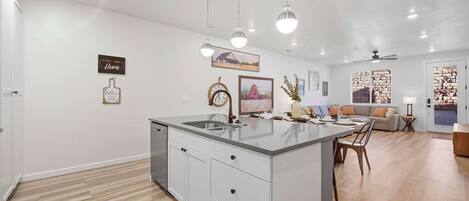 Cozinha moderna com ilha central, iluminação pendente e área de refeições com sofá e mesa.
