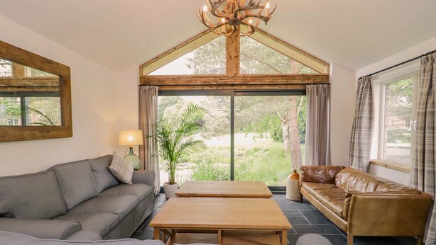 A room with a grey sofa, a brown leather sofa, a wooden coffee table, and a chandelier.