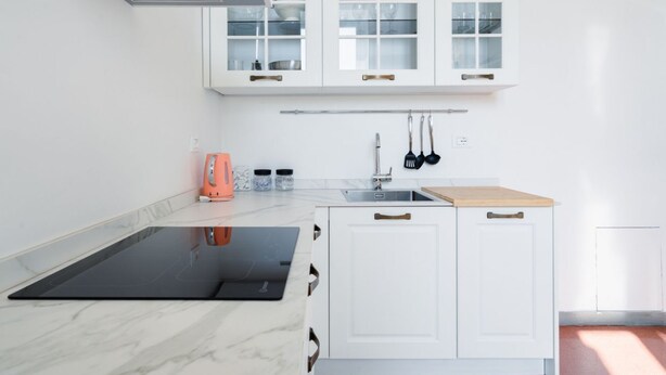 Una cocina moderna con armarios blancos, una placa de inducción negra y una encimera de madera.