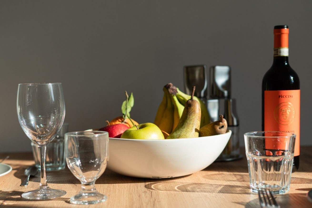 A table with a bowl of fruit, a wine bottle, and empty glasses.