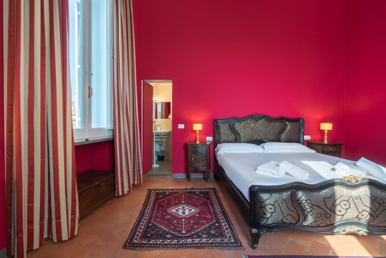 A bedroom with a bed, a nightstand, a lamp, a window with curtains, and a rug.