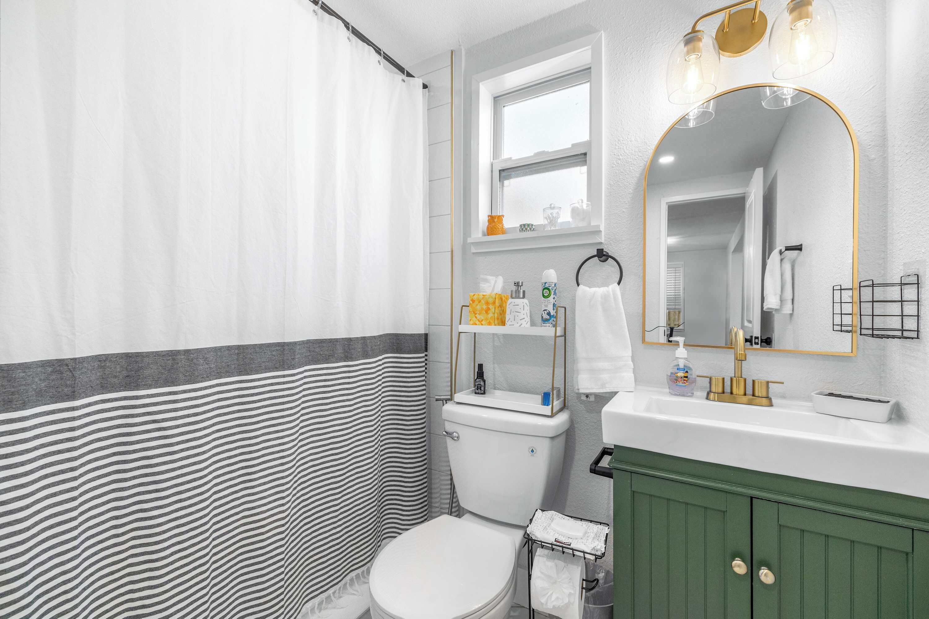 Un baño con cortina de ducha a rayas, un inodoro, un lavabo con espejo y un armario verde.
