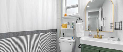 Un baño con cortina de ducha a rayas, un inodoro, un lavabo con espejo y un armario verde.