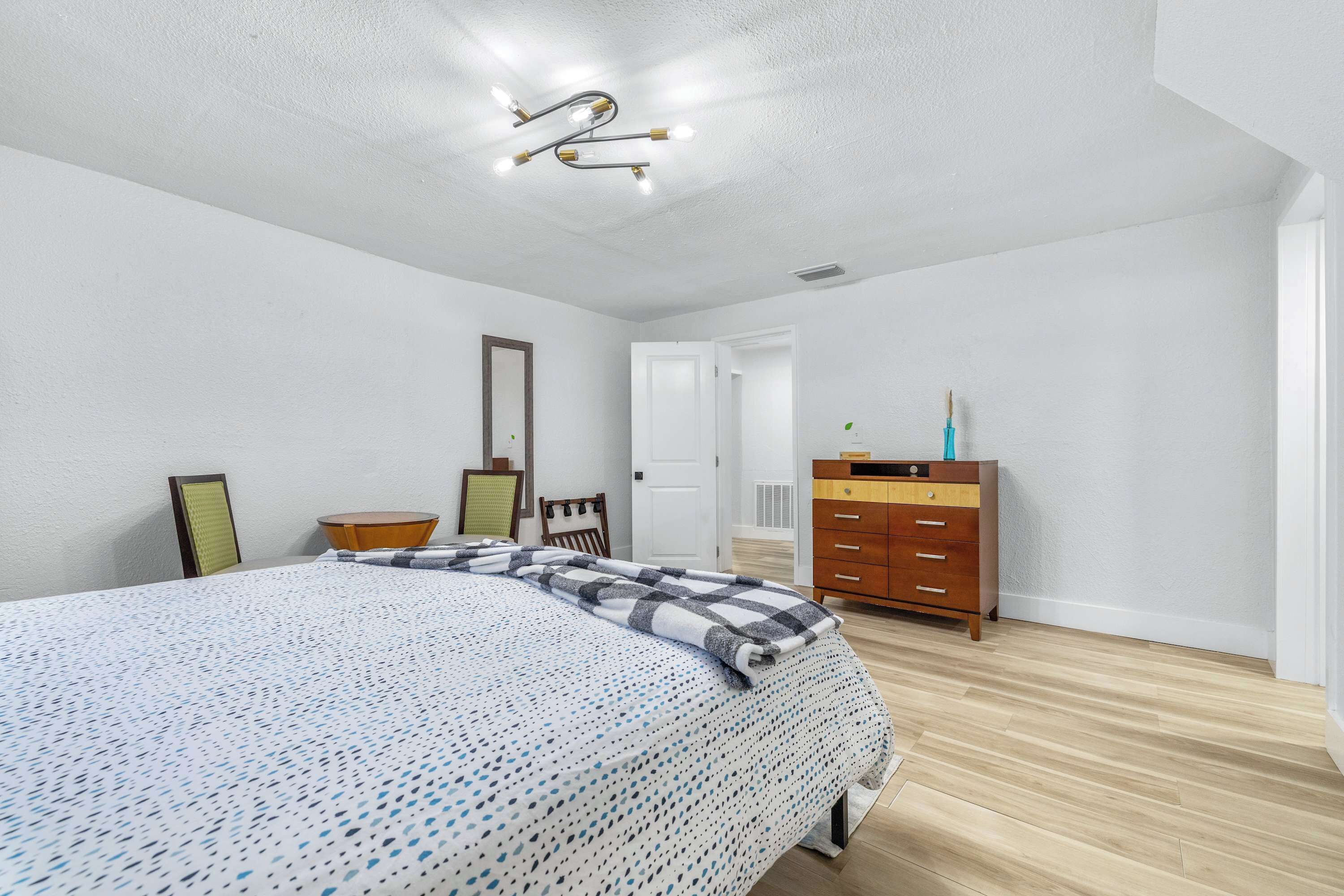 Une chambre à coucher avec un grand lit, une commode en bois, une chaise et une porte donnant sur une autre pièce.