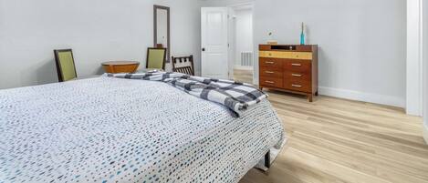 Une chambre à coucher avec un grand lit, une commode en bois, une chaise et une porte donnant sur une autre pièce.