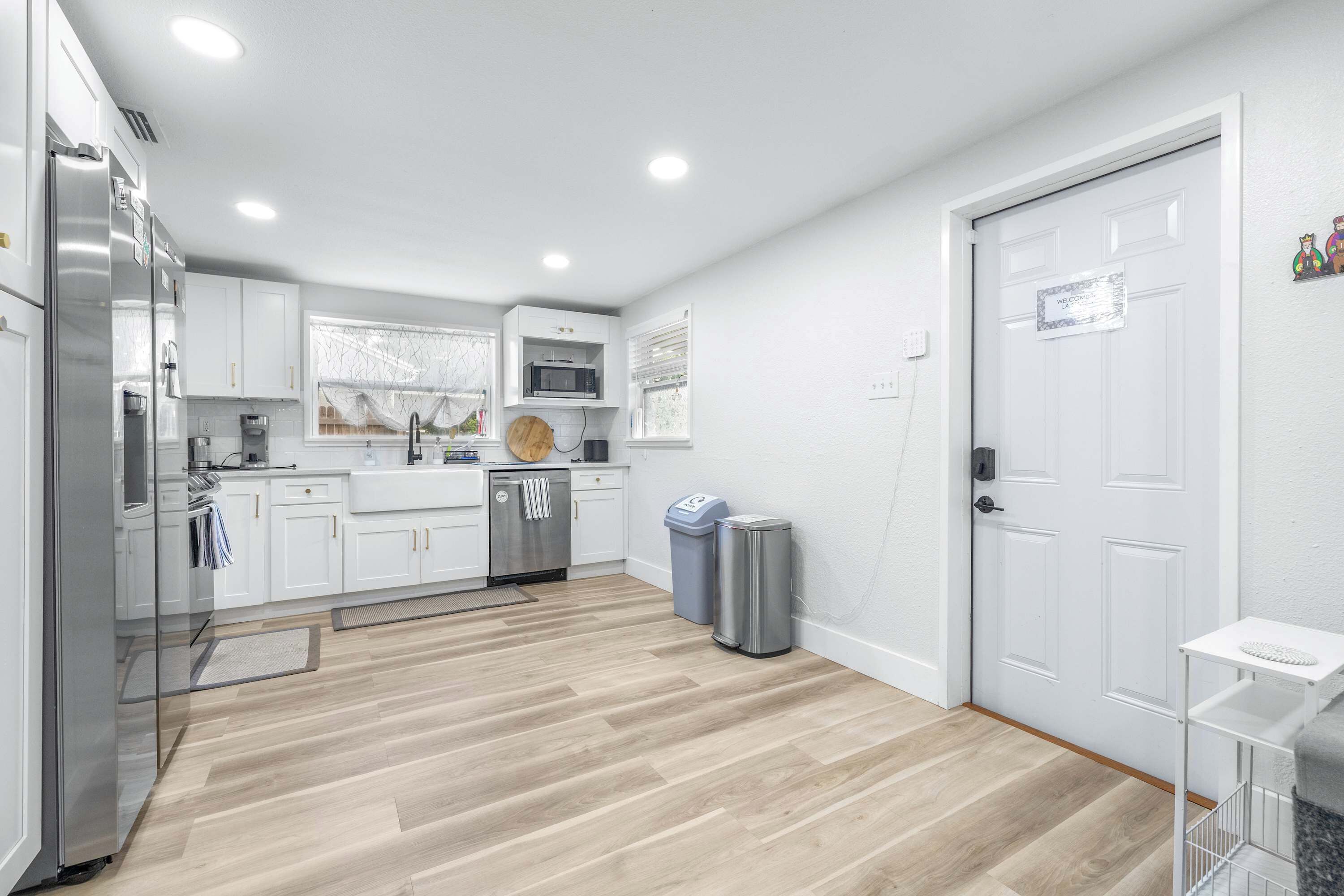 A modern kitchen with white cabinets, stainless steel appliances, and a herringbone wood floor.