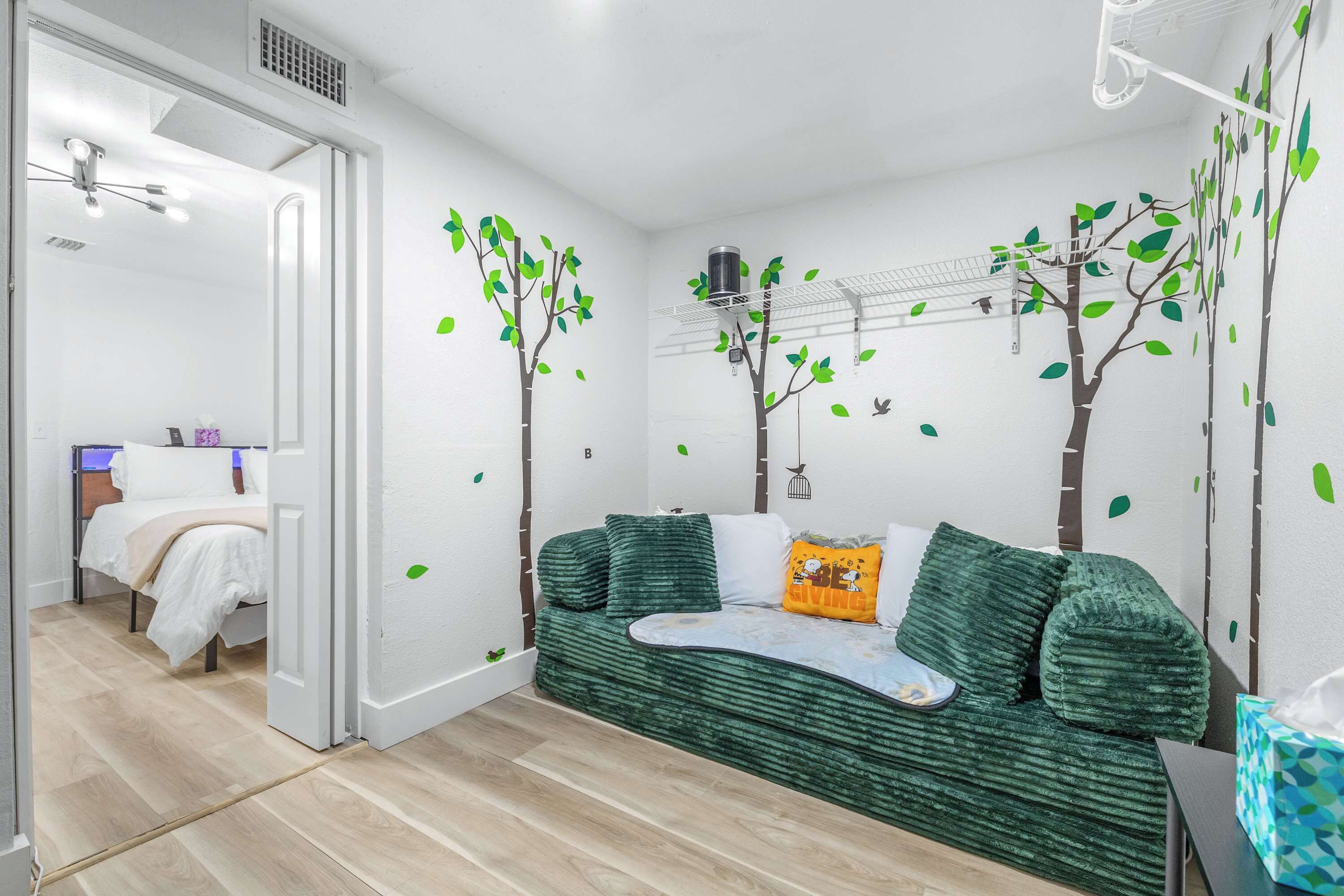 Una habitación con un sofá verde, una cama y una pared decorada con motivos de árboles.