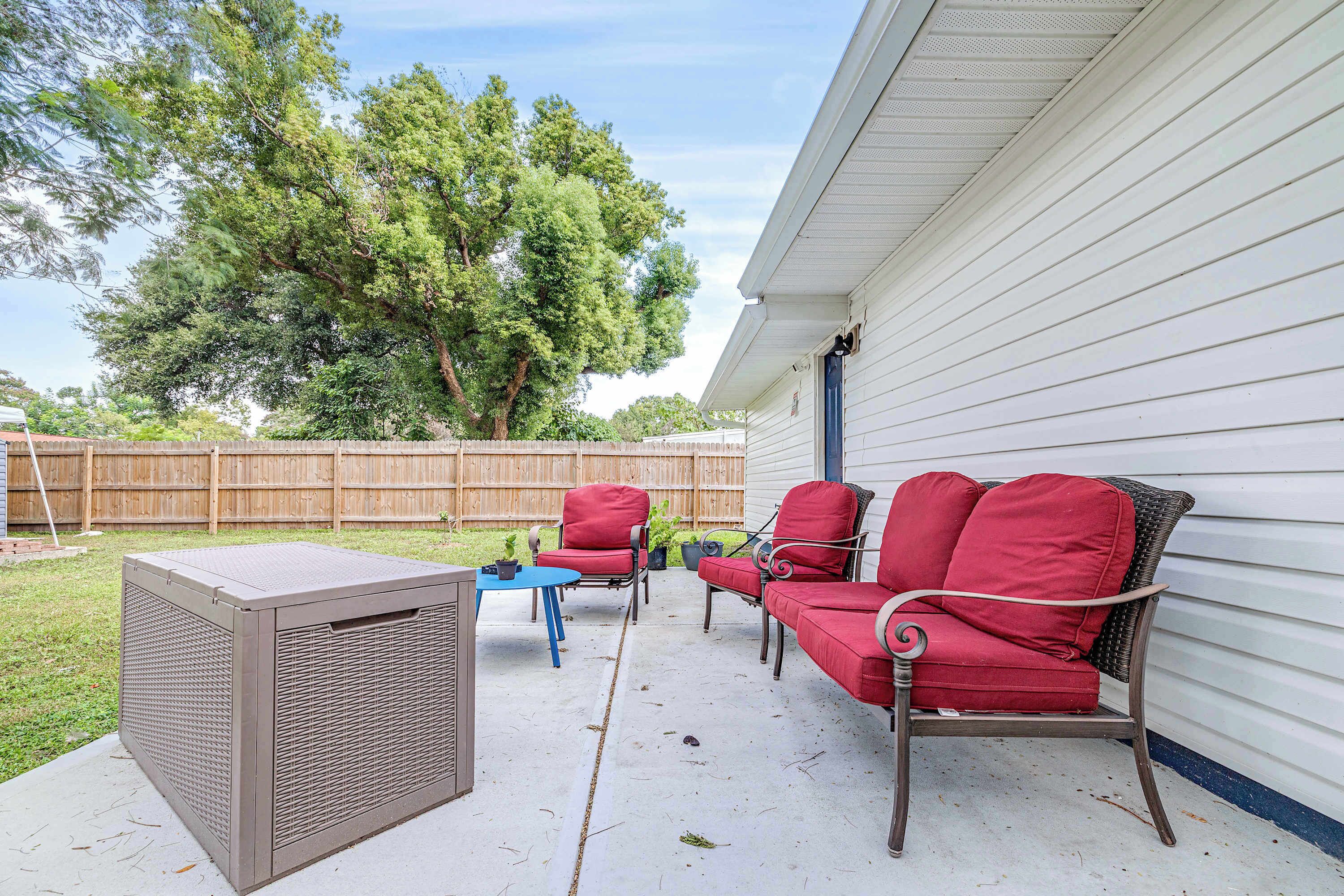 An outdoor patio with a metal air conditioning unit, a blue table, and red wicker furniture.