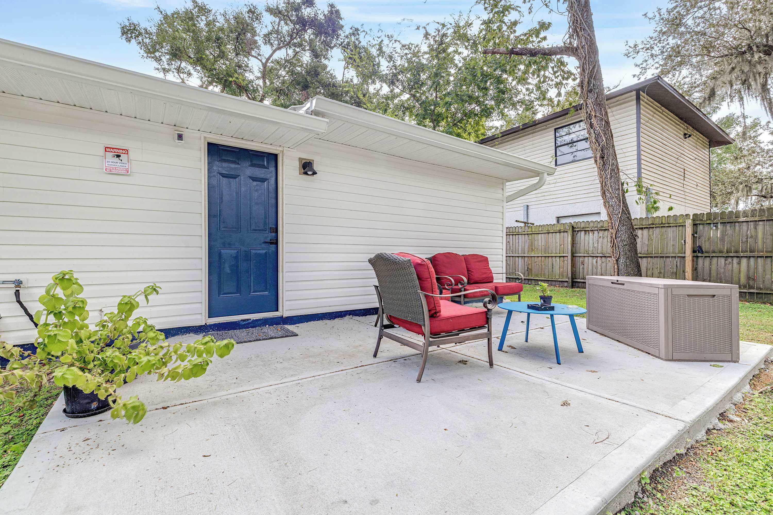 A small, single-story building with a blue door, a red chair, a small table, and a large air conditioning unit.