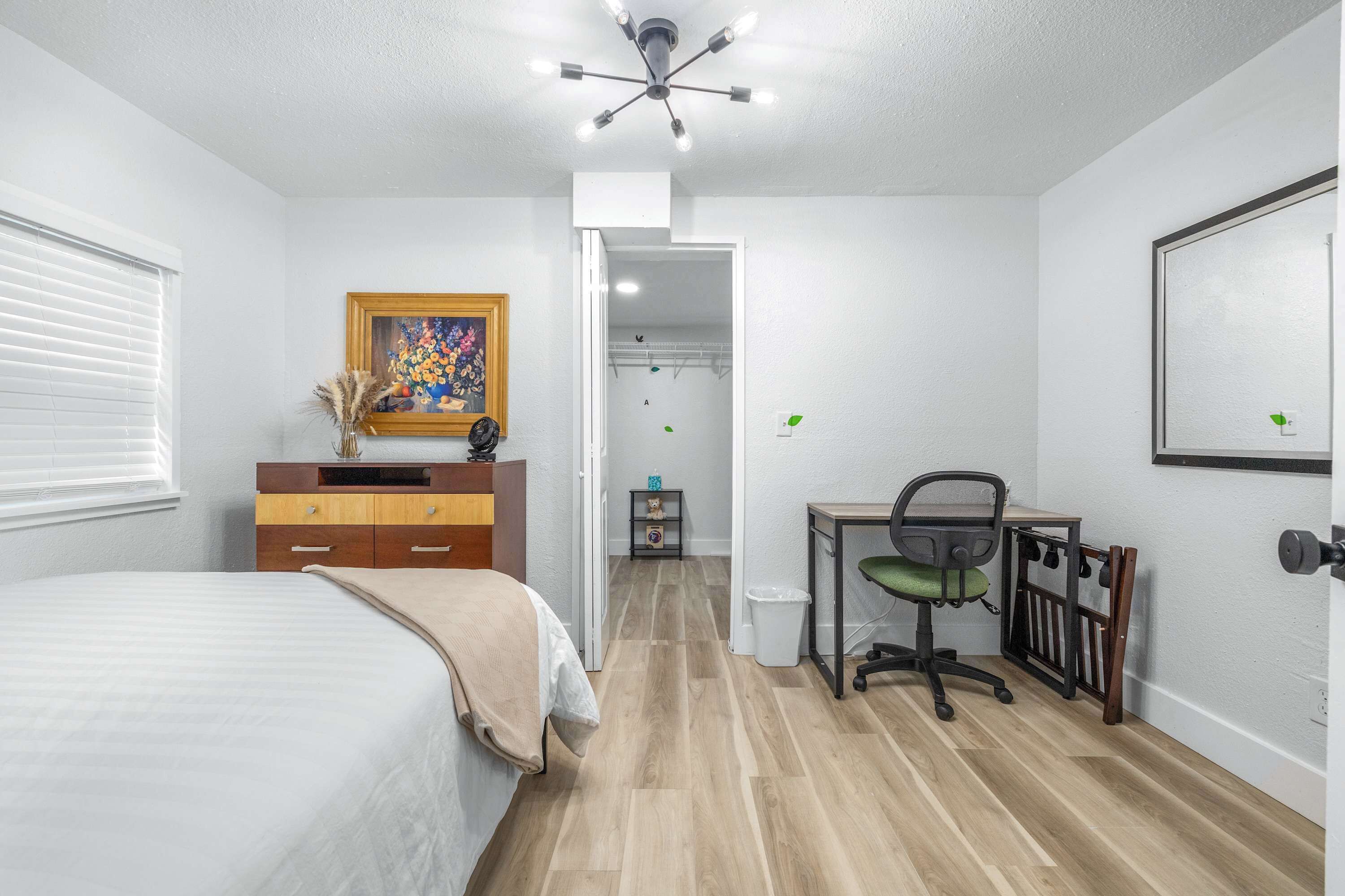 A bedroom with a bed, a desk, a chair, a wardrobe, and a door leading to a closet.