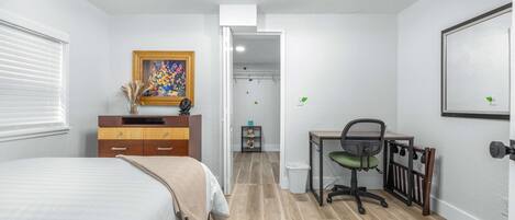 A bedroom with a bed, a desk, a chair, a wardrobe, and a door leading to a closet.