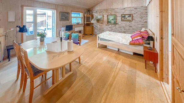 A cozy room with a wooden floor, a bed with colorful pillows, a dining table with chairs, a TV, and a cabinet with a lamp. - 1 bedroom lovely home in Vig (Vig)