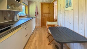 A compact kitchen with a wooden interior, a sink, a stove, and a dining area with a table and chairs. - 1 bedroom lovely home in Vig (Vig)