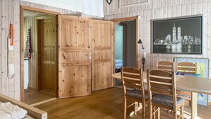 A room with wooden walls and floors, a dining table with chairs, a bed with a white mattress, and a framed cityscape picture on the wall. - 1 bedroom lovely home in Vig (Vig)