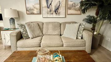 Un salon avec un canapé beige, trois tableaux représentant des oiseaux, une table basse en bois ornée de vases décoratifs et une plante en pot.