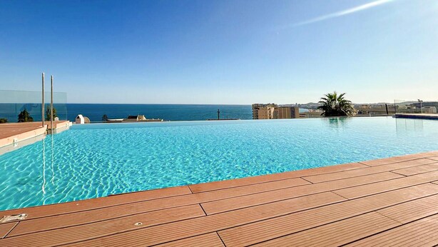 Una piscina cristallina con un pontile in legno, con vista sul mare.