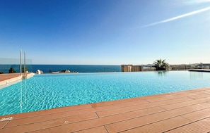 Une piscine d’un bleu éclatant, bordée d’une terrasse en bois, qui offre une vue sur la mer.