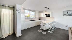 Una cucina moderna con mobili bianchi, un'ampia finestra e un'area pranzo con sgabelli da bar.