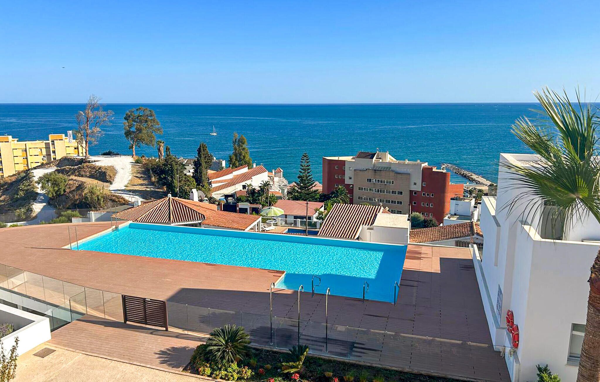 A rooftop pool with a view of the sea, surrounded by buildings and greenery.