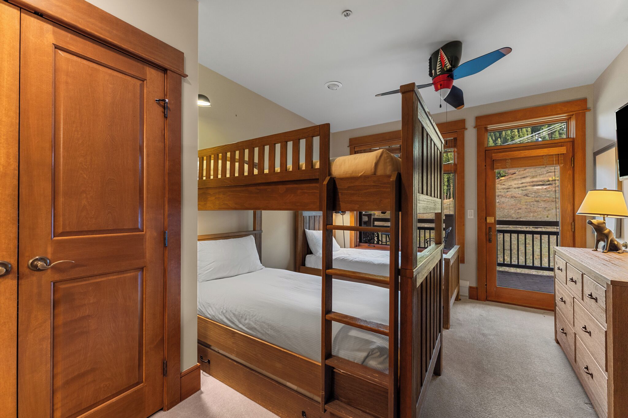 A bedroom with a bunk bed, wooden wardrobe, and a ceiling fan.