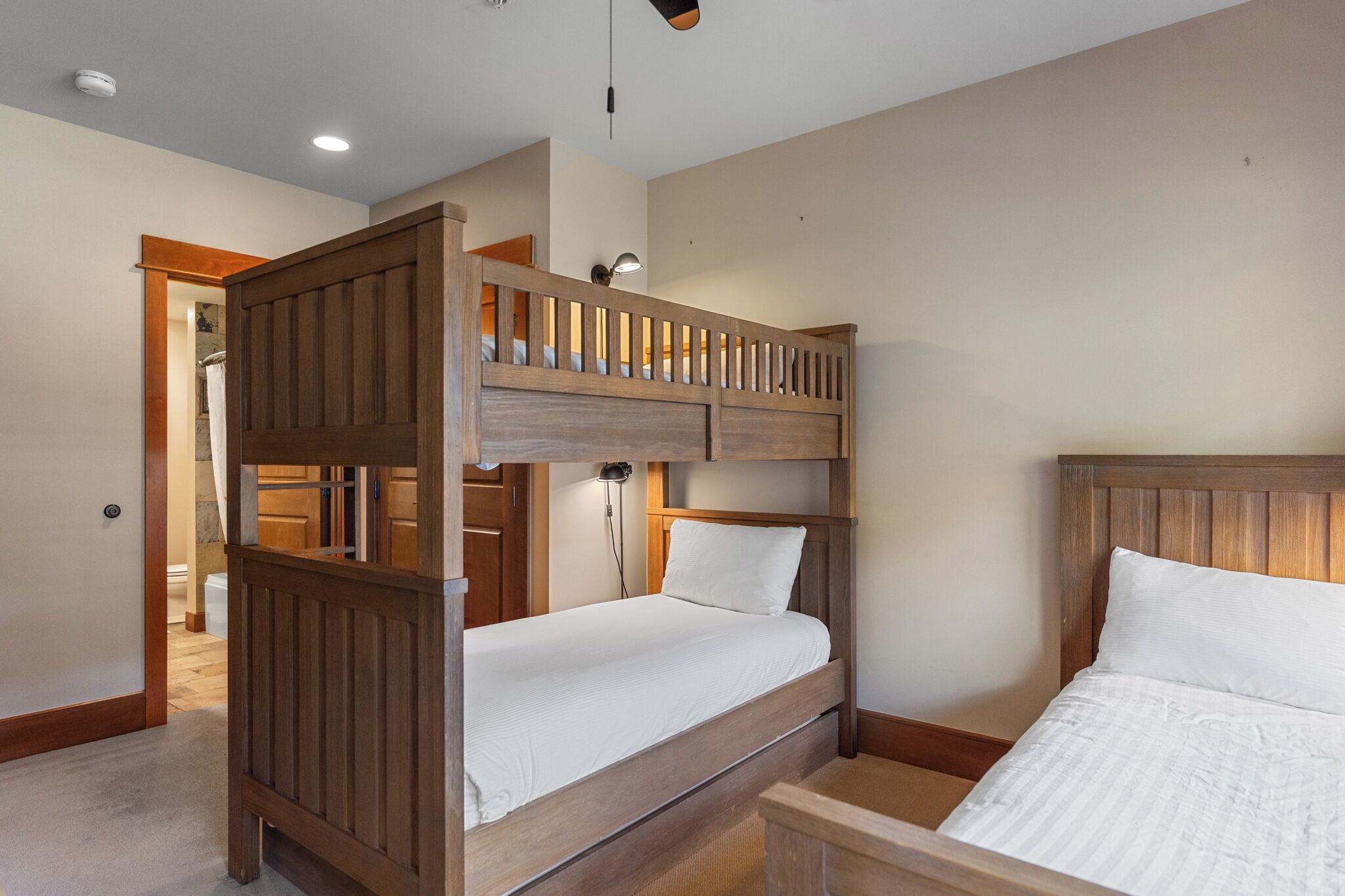 A bunk bed room with wooden headboards, a bedside table, and a door leading to a bathroom.