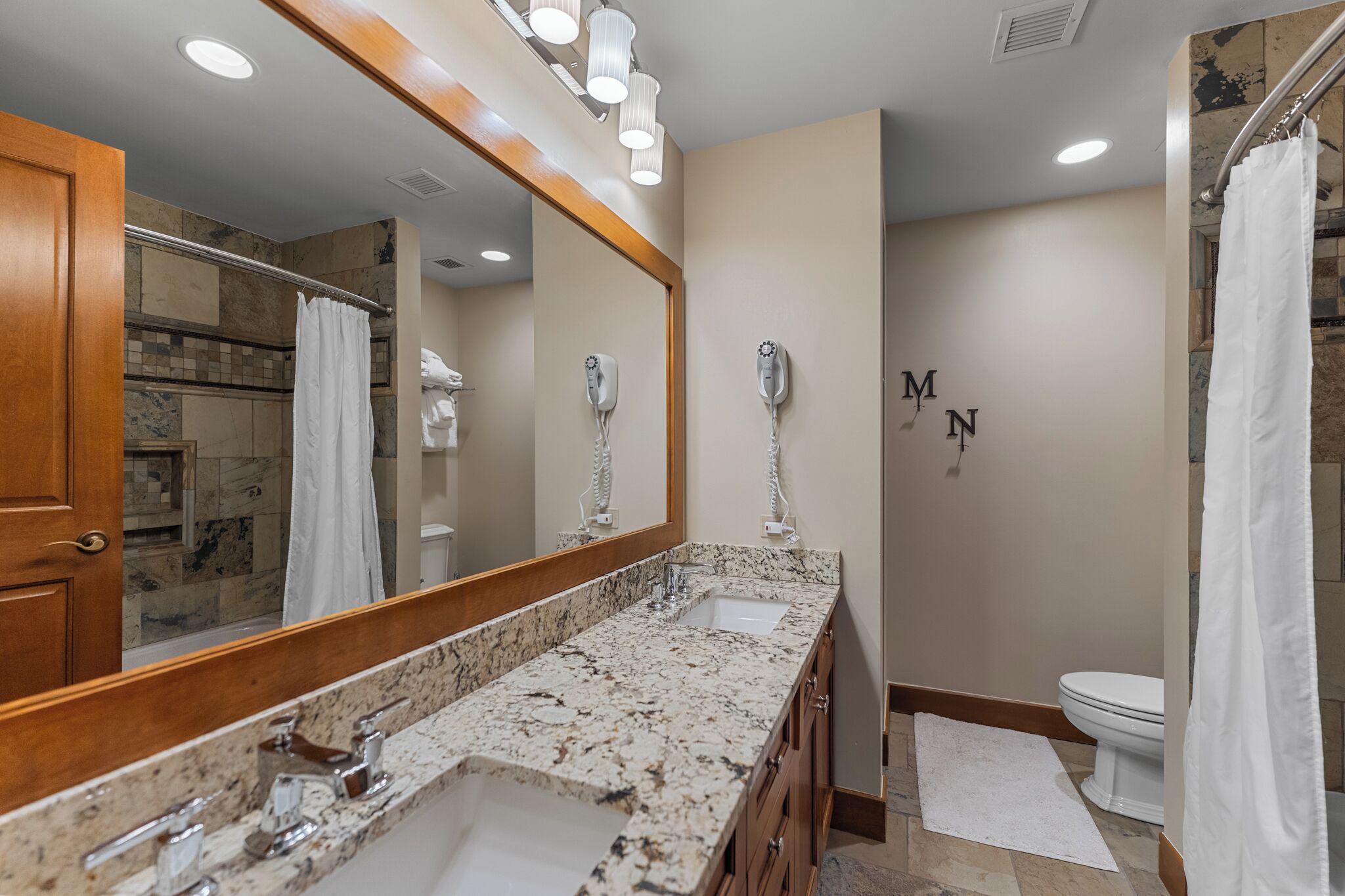 A bathroom with a marble countertop, a large mirror, a shower, and a toilet.