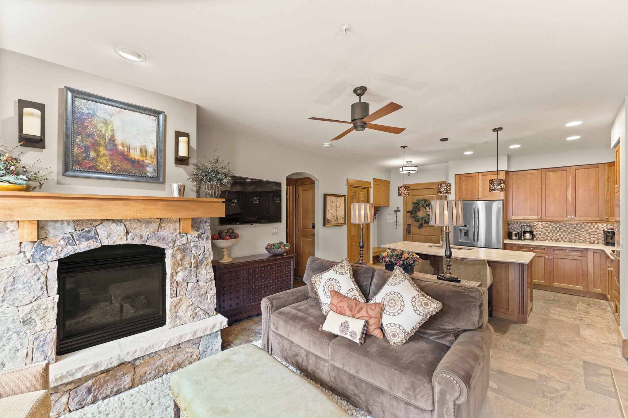 A living room with a stone fireplace, a sofa, and a TV mounted above it.