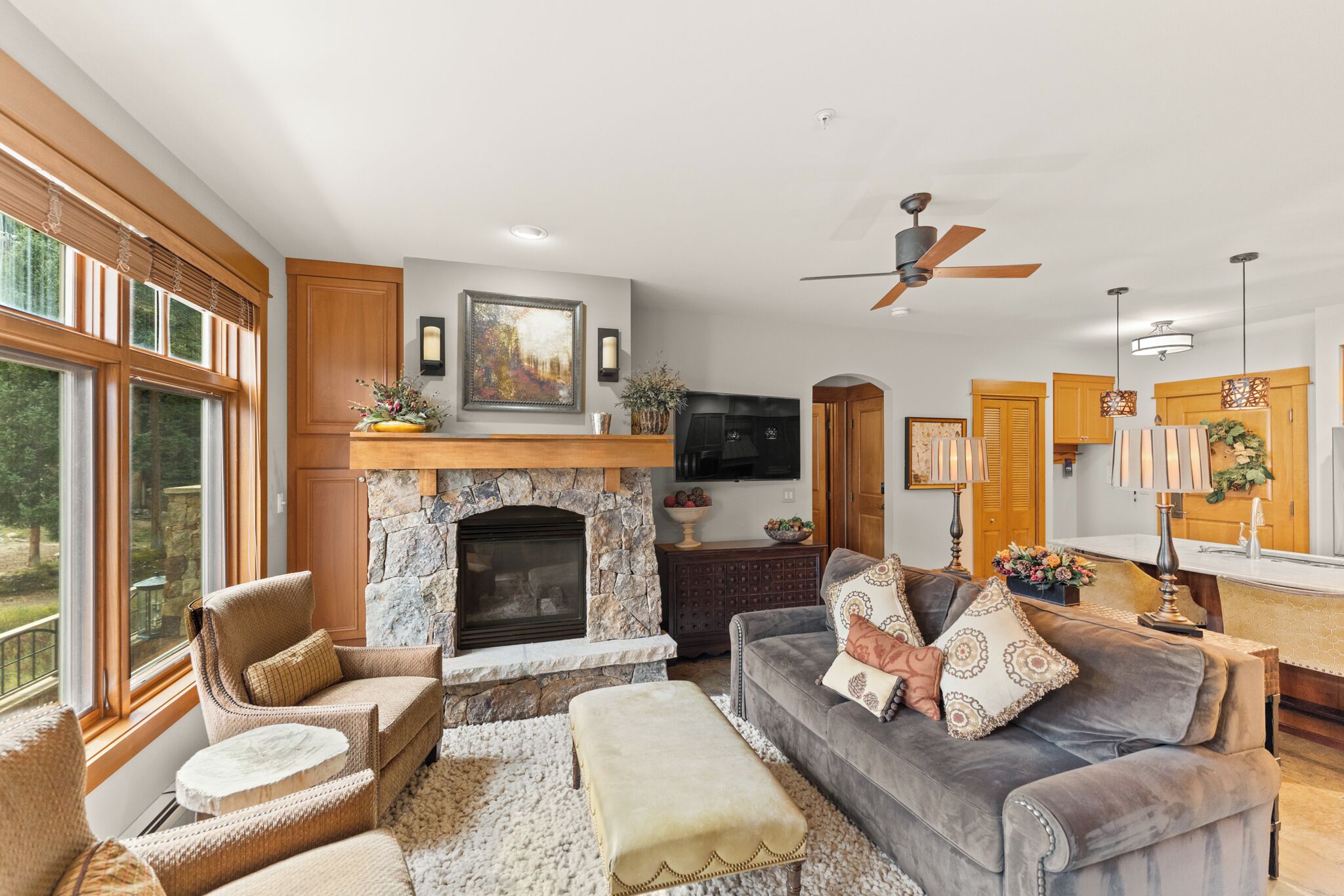 A spacious living room with a stone fireplace, comfortable seating, and a large window offering a view of the outdoors.