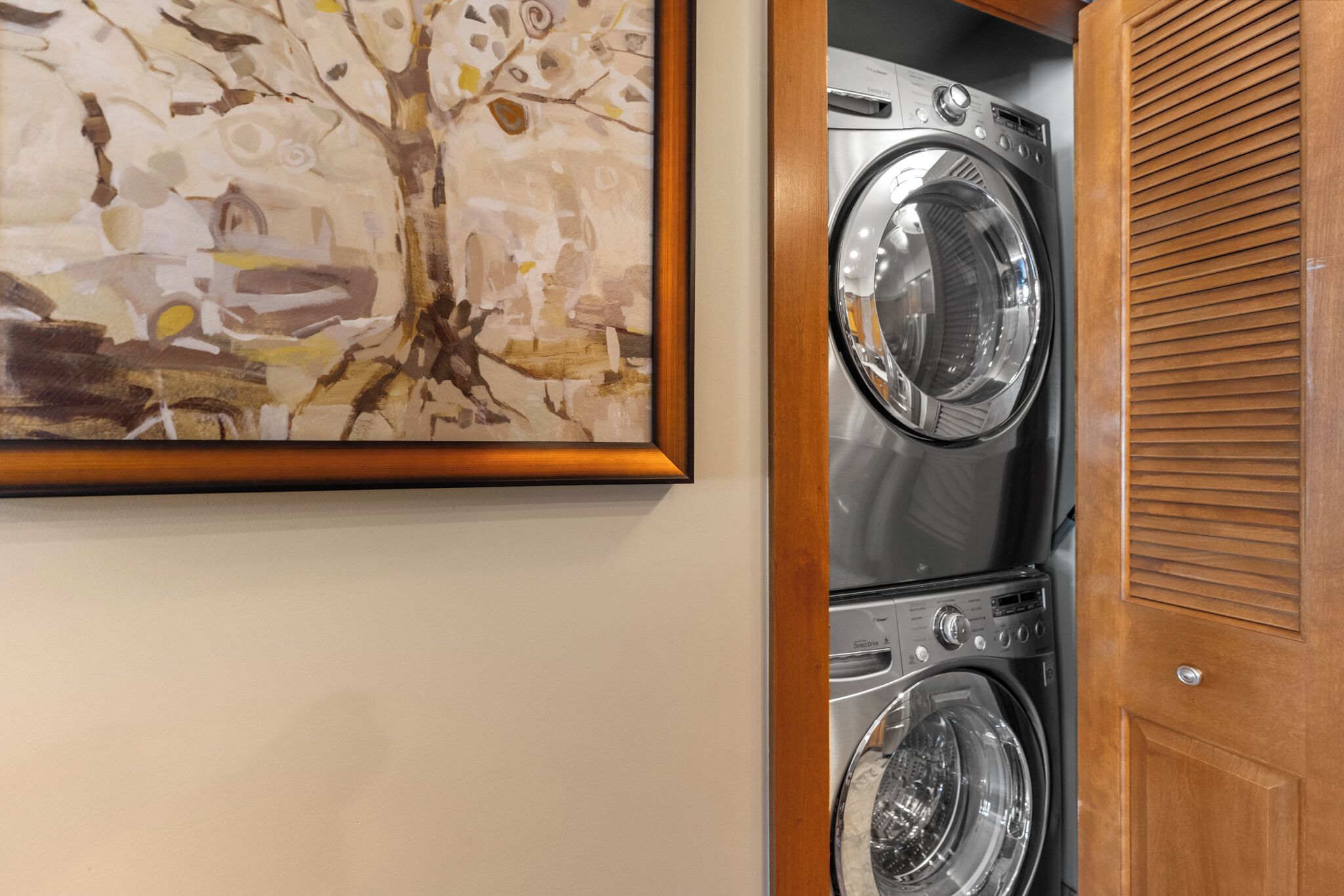 A laundry room with stacked washers and dryers, a wooden door, and a framed abstract painting on the wall.