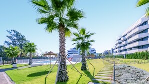 A modern building with a pool area, palm trees, and a well-maintained lawn.