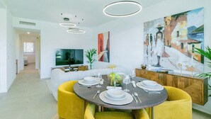 A modern dining area with a round table, yellow chairs, and a TV in the background.