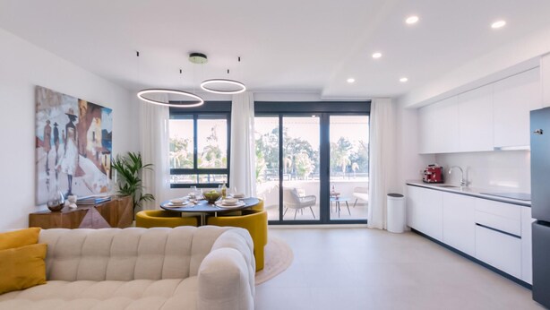 A modern living room with a sofa, a dining area with a table and chairs, and a kitchen with white cabinets and a sink.