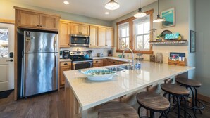 A modern kitchen with wooden cabinets, stainless steel appliances, a large island with stools, and pendant lighting. - Lookout Chelan: PVT Hot Tub, Family Friendly, Outdoor Games, Vineyard Park Home, (Chelan)