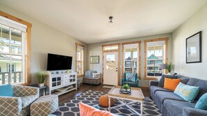 A spacious living room with a large flat-screen TV, a grey sofa, a blue armchair, and a coffee table with a plant. - Lookout Chelan: PVT Hot Tub, Family Friendly, Outdoor Games, Vineyard Park Home, (Chelan)