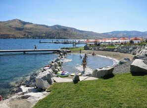 A lakeside resort with a swimming area, a dock, and a view of distant hills.