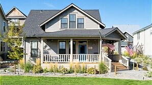 A two-story house with a front porch, a small deck, and a flag. - Lookout Chelan: PVT Hot Tub, Family Friendly, Outdoor Games, Vineyard Park Home, (Chelan)