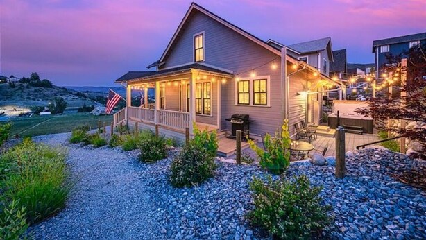 A two-story house with a porch, outdoor seating, and a view of the surrounding landscape. - Lookout Chelan: PVT Hot Tub, Family Friendly, Outdoor Games, Vineyard Park Home, (Chelan)