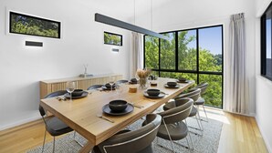 Een moderne eetkamer met een lange houten tafel voor zes personen, omringd door stoelen, met uitzicht op groen door grote ramen.