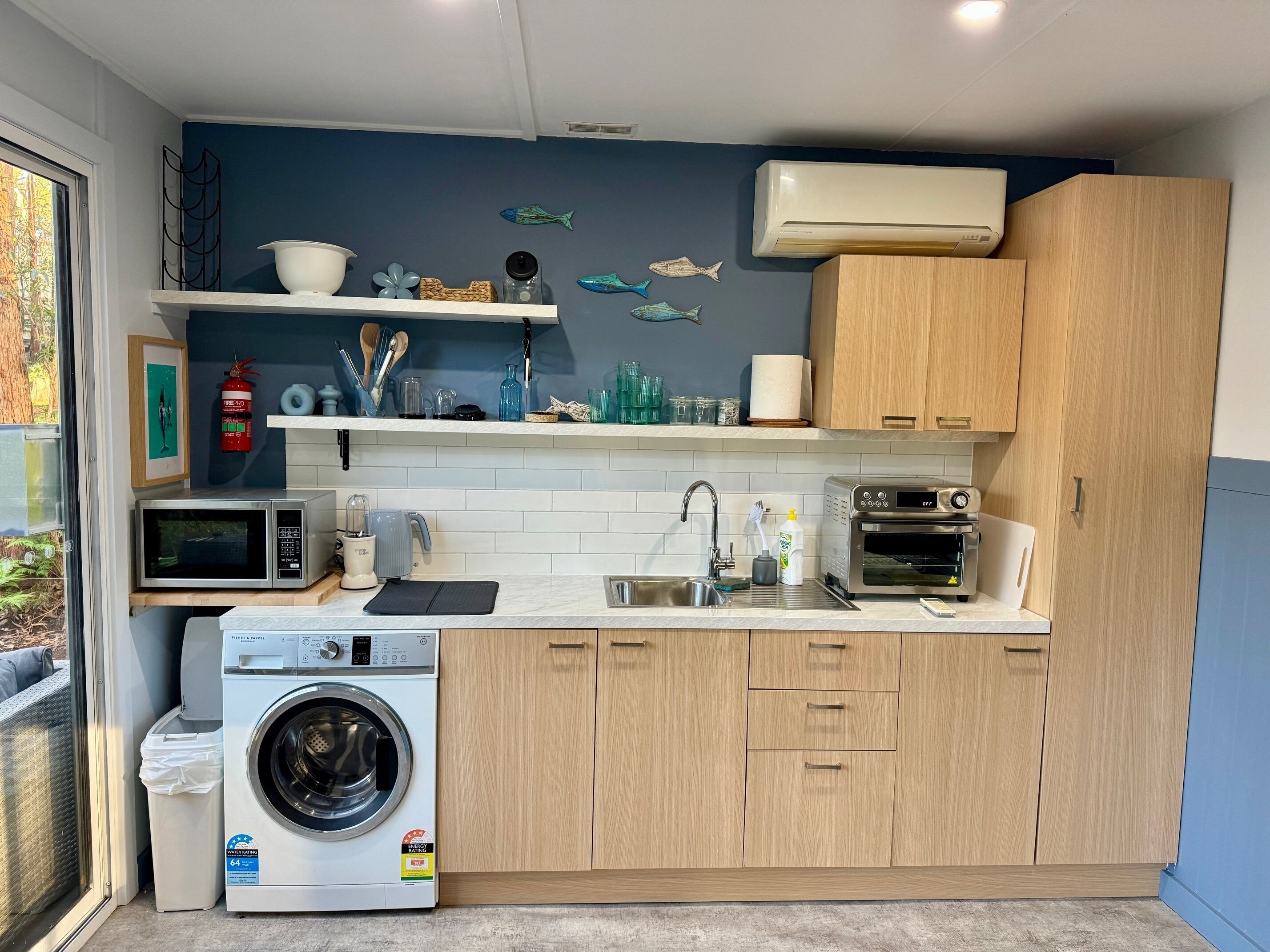 A compact kitchen with a washing machine, microwave, toaster, and a sink.
