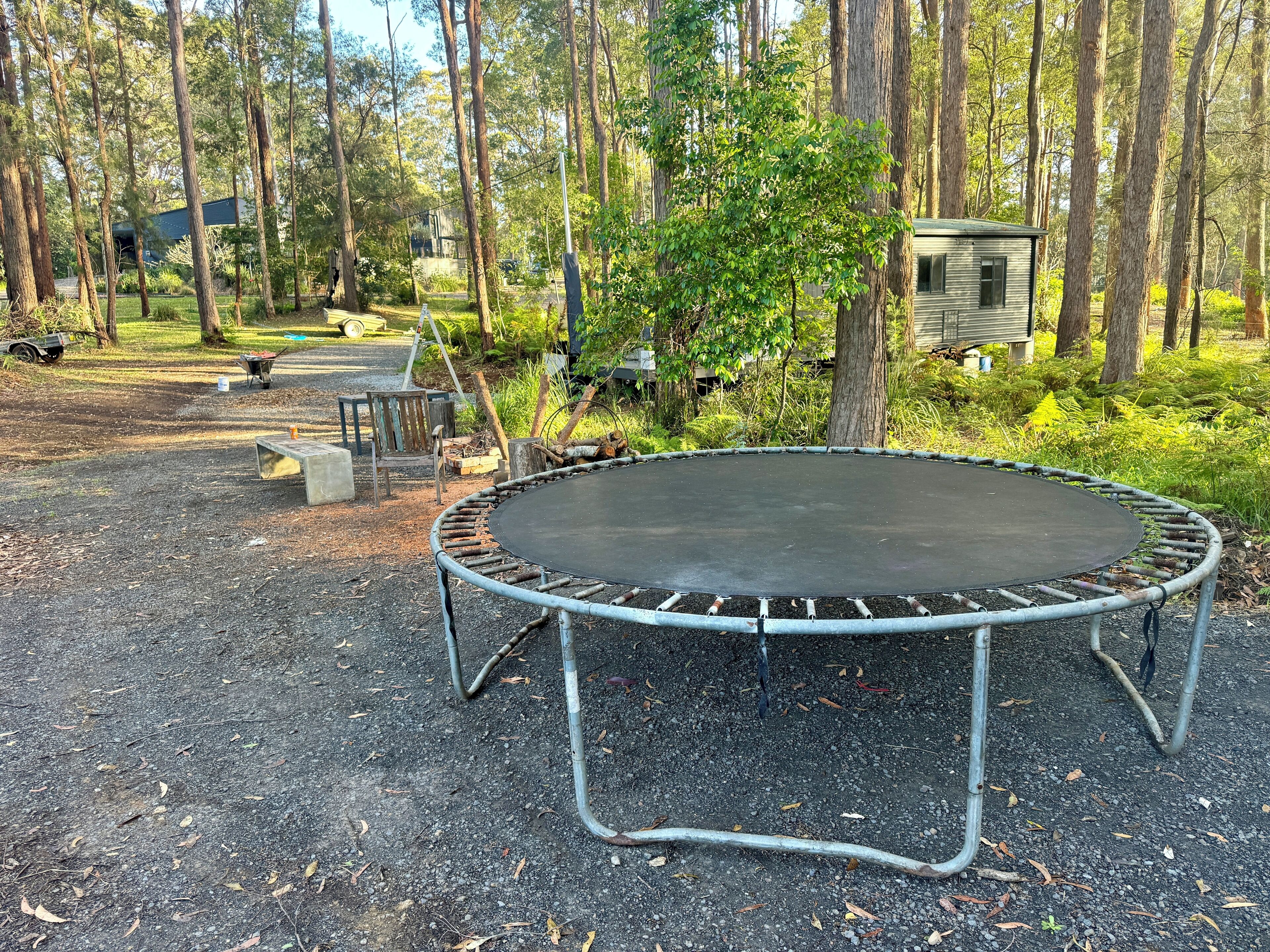 A trampoline surrounded by a forested area with a small wooden cabin in the background.
