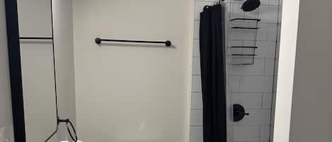 Un baño moderno con un lavamanos blanco, un grifo negro y un inodoro blanco. Hay una cortina de ducha negra y un perchero negro.